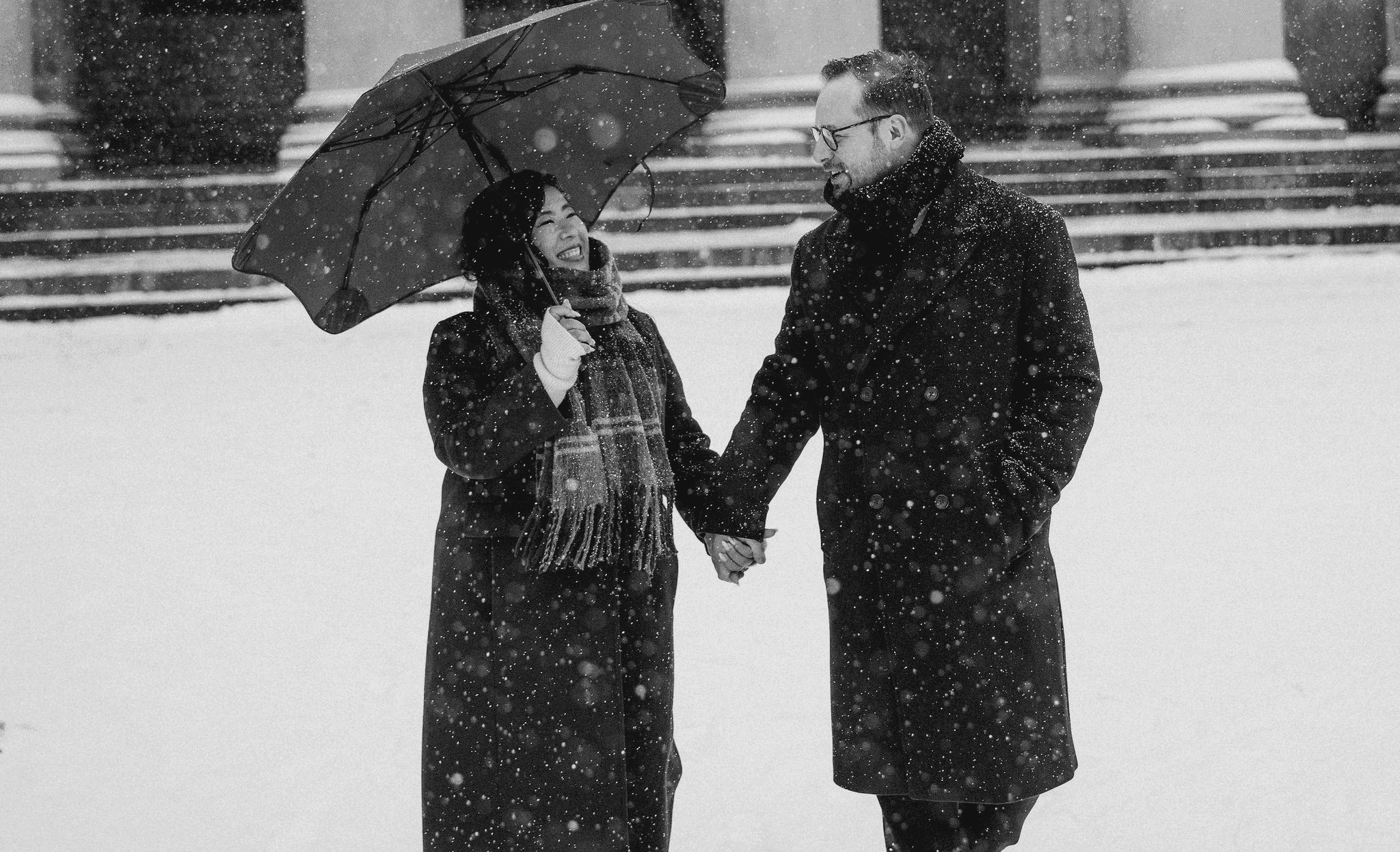 Sarah and Mark holding hands under an umbrella in the snow